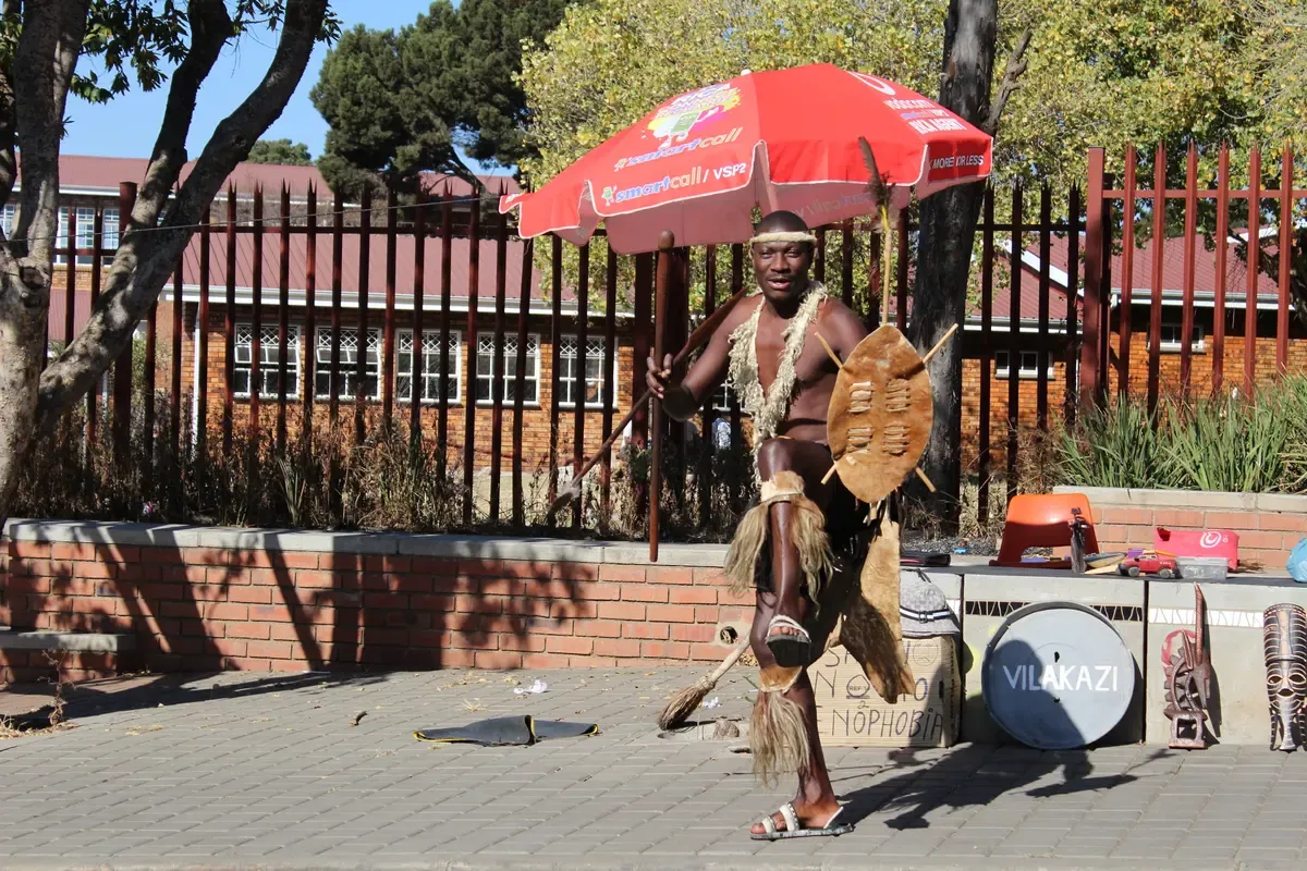A street performer on Vilakazi Street in Soweto, the trees and small houses of the famous street behind him
